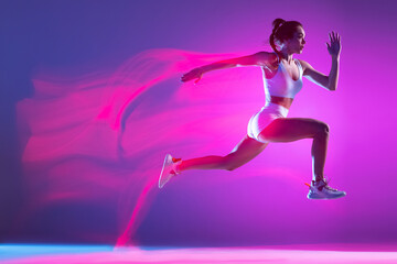 Fototapeta na wymiar Professional female athlete, runner training isolated on blue studio background in mixed pink neon light. Healthy lifestyle, sport, motion and action concept.
