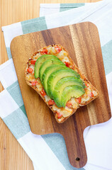 Top view of homemade grilled cheese toast with sliced avocado and tomato on wooden breadboard