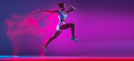 Flyer with professional female athlete, runner training isolated on blue studio background in mixed pink neon light. Sport, motion and action concept.