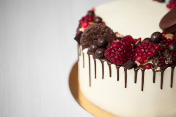 cake with white cream, chocolate drips, pomegranate, nuts and chocolate decor