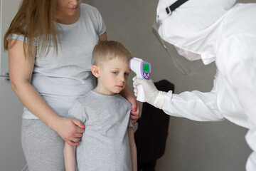 Pediatrician or doctor checks elementary age boy's body temperature using infrared forehead...