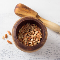 Wooden mortar with almonds and a wooden pestle on a light gray background