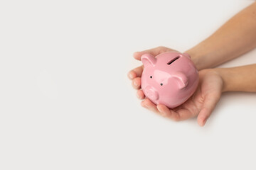 Child's hand is holding a white piggy bank on white background. Saving money concept for the...