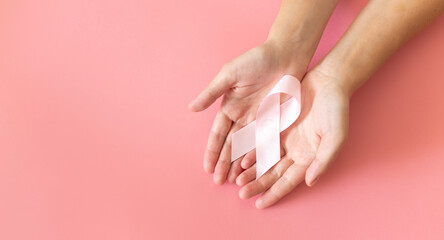 Hands holding pink ribbon on pink background, Breast cancer awareness and October Pink day, world cancer day, national cancer survivor day