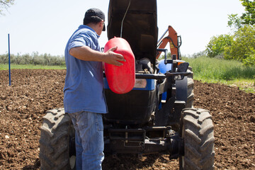 Farmer putting diesel fuel to the tractor with a jerrycan. Reference to expensive fuel in the...