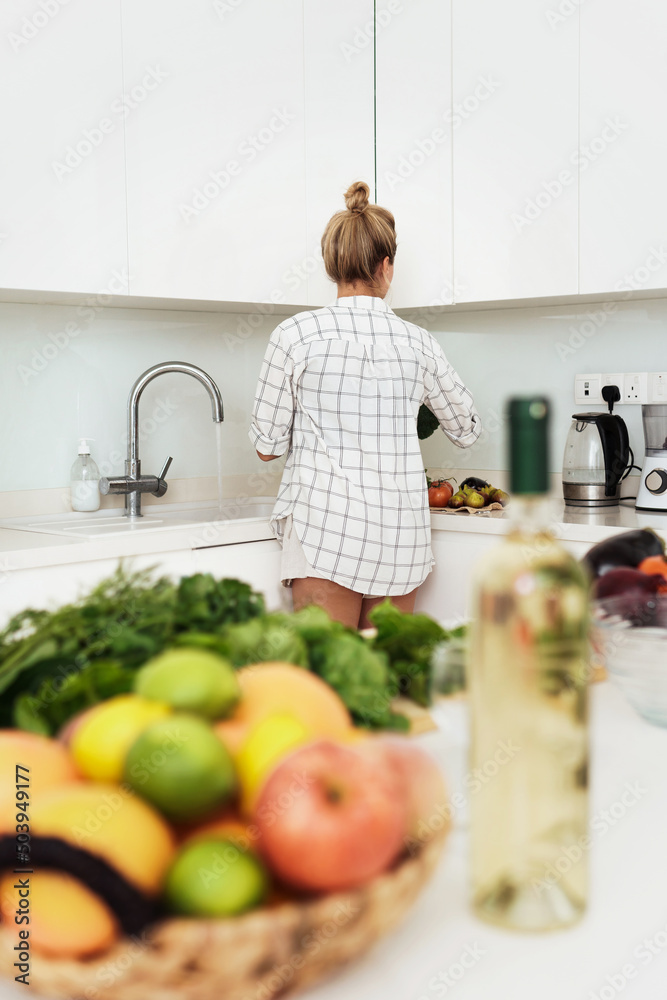 Wall mural Woman washing vegetables before meal cooking in white modern kitchen