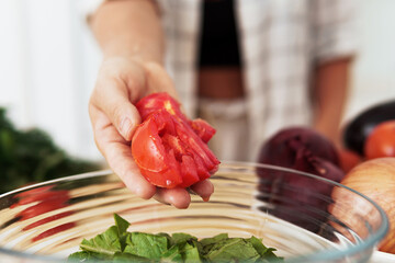 Female hand with sliced tomato and bowl with lettuce salad