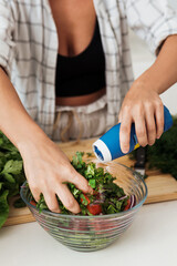 Female hands mixing vegetarian salad and adding the salt to it