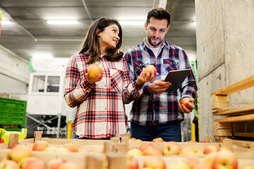Two supervisors looking at the apples in food factory and assessing quality on tablet.