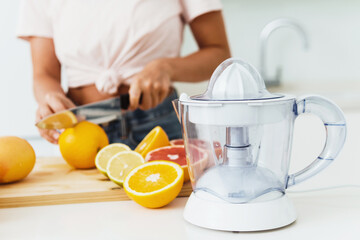 Juicer and young woman is cutting citrus fruits for homemade fresh juice