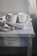 Two corrugated mugs on a white tray and a kitchen towel on a beige table against a white wall. Scandinavian style. Minimalism. Place for text