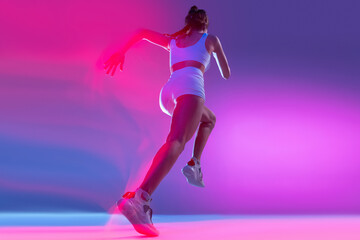 Fototapeta na wymiar Professional female athlete, runner training isolated on blue studio background in mixed pink neon light. Healthy lifestyle, sport, motion and action concept.