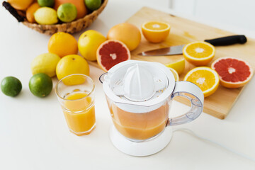 Glass of orange juice, citrus juicer and various citrus fruits on kitchen table
