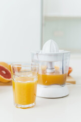 Glass of orange juice, citrus juicer and various citrus fruits on kitchen table