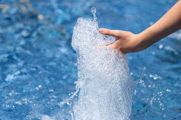 Splash of a jet of clean water from a fountain pouring into the hands of a child.