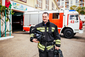 Fototapeta premium Firefighters man in a protective suit near fire truck. Protection, rescue from danger. Fire station