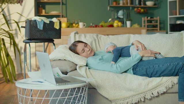 Business Mother tired with kid. Woman Sleeping During Work With the Child on the Hands From Home.Stressed Mom at Home Office. Candid authentic and real-life mom working.