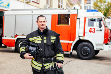 Fototapeta premium Firefighters man in a protective suit near fire truck. Protection, rescue from danger. Fire station