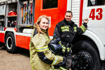 Fototapeta na wymiar Firefighters woman and man in helmets near fire truck. Protection, rescue from danger. Fire station
