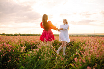Fototapeta premium Portrait of two young woman in stylish dress posing in the blooming field. Nature, vacation, relax and lifestyle. Fashion concept.