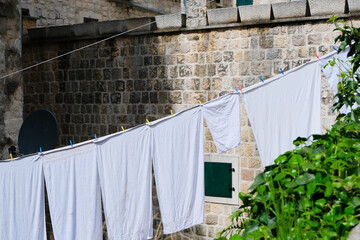 white clean laundry drying on a clothesline outdoor in the sun at the old stone wall background, creative cleaning pattern with copy space	
