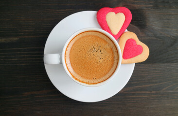 Top view of frothy espresso coffee with a pair of heart shaped cookies on black wooden background