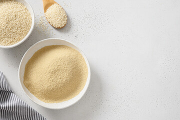 Sesame flour in bowl and white sesame seeds in wooden spoon on white background. View from above. Copy space. Good vegan source of protein, minerals, natural antioxidants and vitamins.