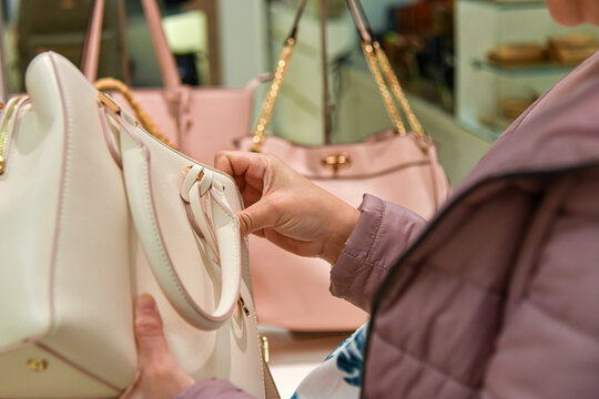 A woman chooses leather handbags for sale in a shopping mall.