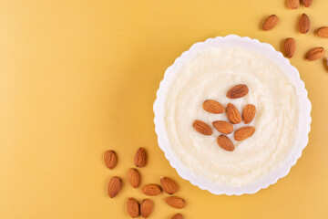 Semolina porridge with almonds in a beautiful white plate on a yellow background. Place for text, recipe.