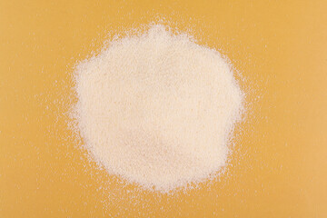 A handful (pile) of dry semolina on a yellow background close-up.