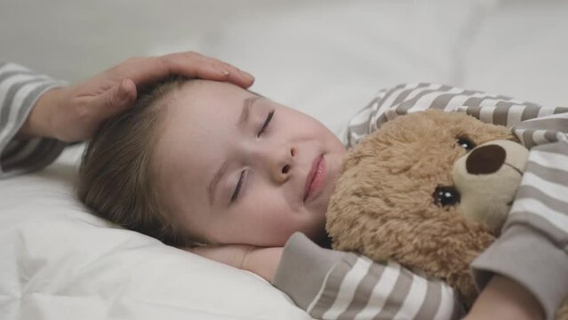little child kid falls asleep mom lap hugging teddy bear. happy girl goes bed. mom strokes child daughter head. toy teddy bear relaxes kid. evening relaxation bed. health child sleep. mother care