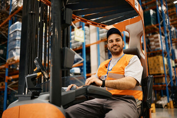 Happy forklift operator working at distribution warehouse and looking at camera. - obrazy, fototapety, plakaty