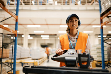 Young woman driving pallet jack while working at distribution warehouse.