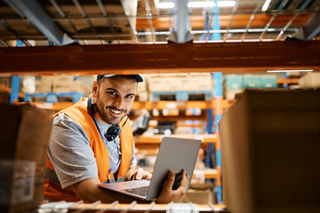 Happy warehouse worker using laptop and looking at camera.