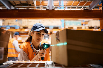 Female warehouse worker uses bar code reader while scanning packages at storage compartment. - obrazy, fototapety, plakaty