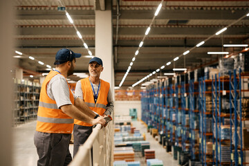 Male warehouse workers talk while working at storage compartment.