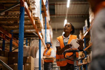 Black female warehouse worker checking stock of merchandise in storage room.