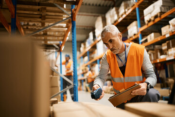 Mature warehouse worker using touchpad and scanning cardboard boxes at storage compartment.