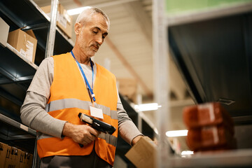Mature warehouse worker scanning packages with bar code reader at storage compartment.