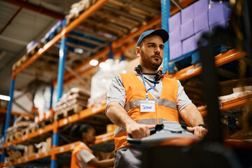 Male worker using pallet jack while working at distribution warehouse.