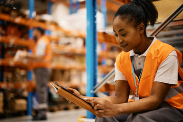 Happy black female warehouse worker surfing the net on touchpad on break.