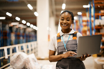 Happy African American warehouse worker using laptop and looking at camera.