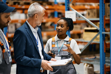 African American warehouse worker and her colleague talking to company manager at storage compartment.