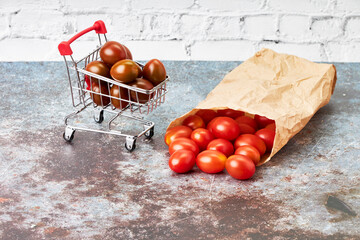 Red cherry tomatoes in a small shopping cart and paper bag. Healthy food shopping. Vegetarian food