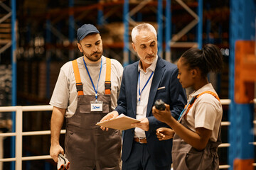 Mature manager talks to warehouse workers at industrial storage compartment. - obrazy, fototapety, plakaty