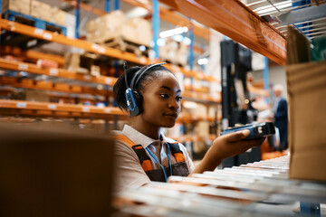 Young black woman scans packages with bar code reader while working at industrial storage...