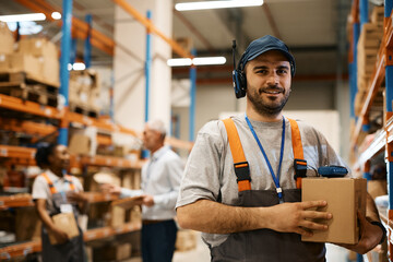 Portrait of happy warehouse dispatcher at storage compartment looking at camera.