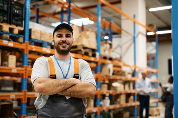 Happy warehouse worker standing with arms crossed and looking at camera.