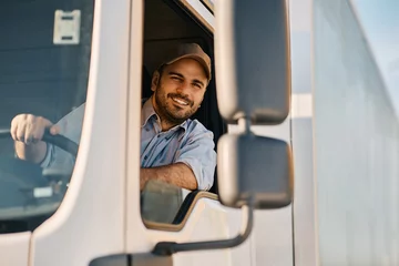 Deurstickers Happy professional truck driver driving his truck and looking at camera. © Drazen
