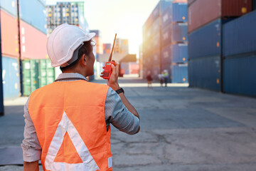 Rear view foreman using walkie talkie radio control loading containers box. Engineer or worker with safety hat work at container cargo site and checking industrial container cargo freight ship.